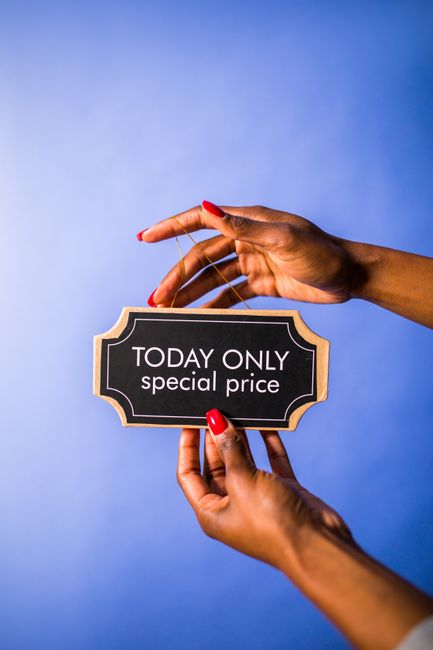 A pair of hands with neatly manicured nails, painted in bright red, are holding a small, black, rectangular sign with a decorative beige border. The sign reads 'TODAY ONLY special price' in white uppercase and lowercase letters. One hand is positioned at the bottom, gripping the sign with fingers gently curved, while the other hand is placed above, supporting the top edge with the index finger and thumb. The background is a smooth, gradient blue that highlights the hands and the sign, creating a clean, professional appearance suitable for a promotional or marketing context related to waste management services like rubbish removal, emphasizing limited-time offers or special pricing. The scene appears well-lit with soft, even lighting, and the hands are visible clearly, showcasing natural skin tone and texture, contributing to an engaging yet neutral visual suitable for accessibility and SEO relevance in promotional content for services such as rubbish removal Kingston.
